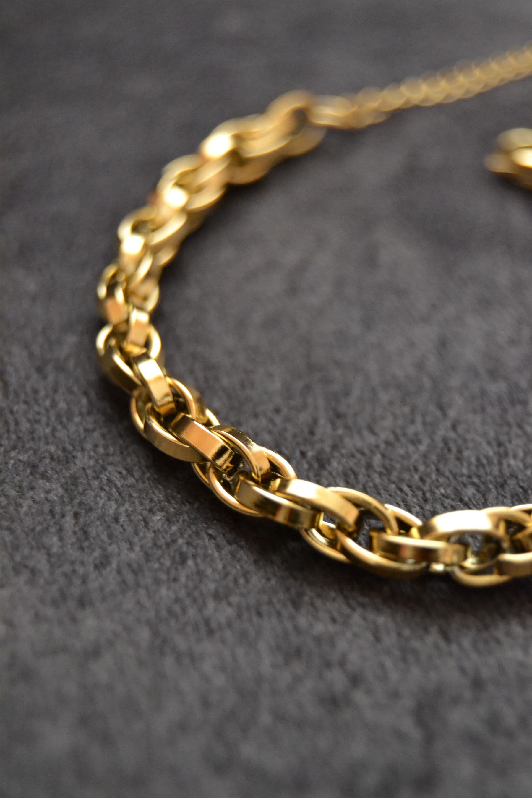 A heavy gold link chain lying on dark grey fabric.