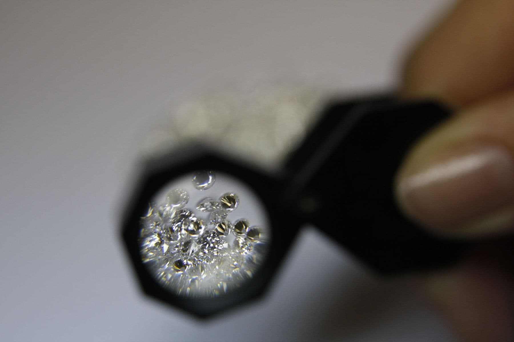Small clear stones seen through a jeweler's loupe held between two fingers.