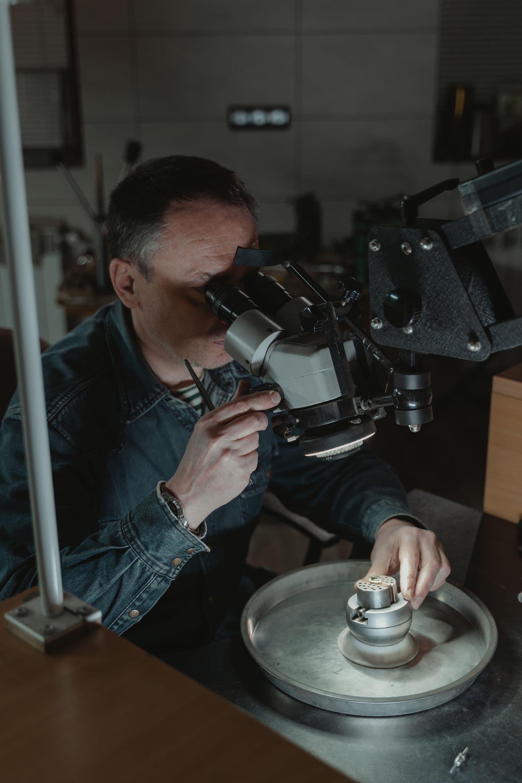 A jeweler looking through a bench microscope at a piece held on a turntable.
