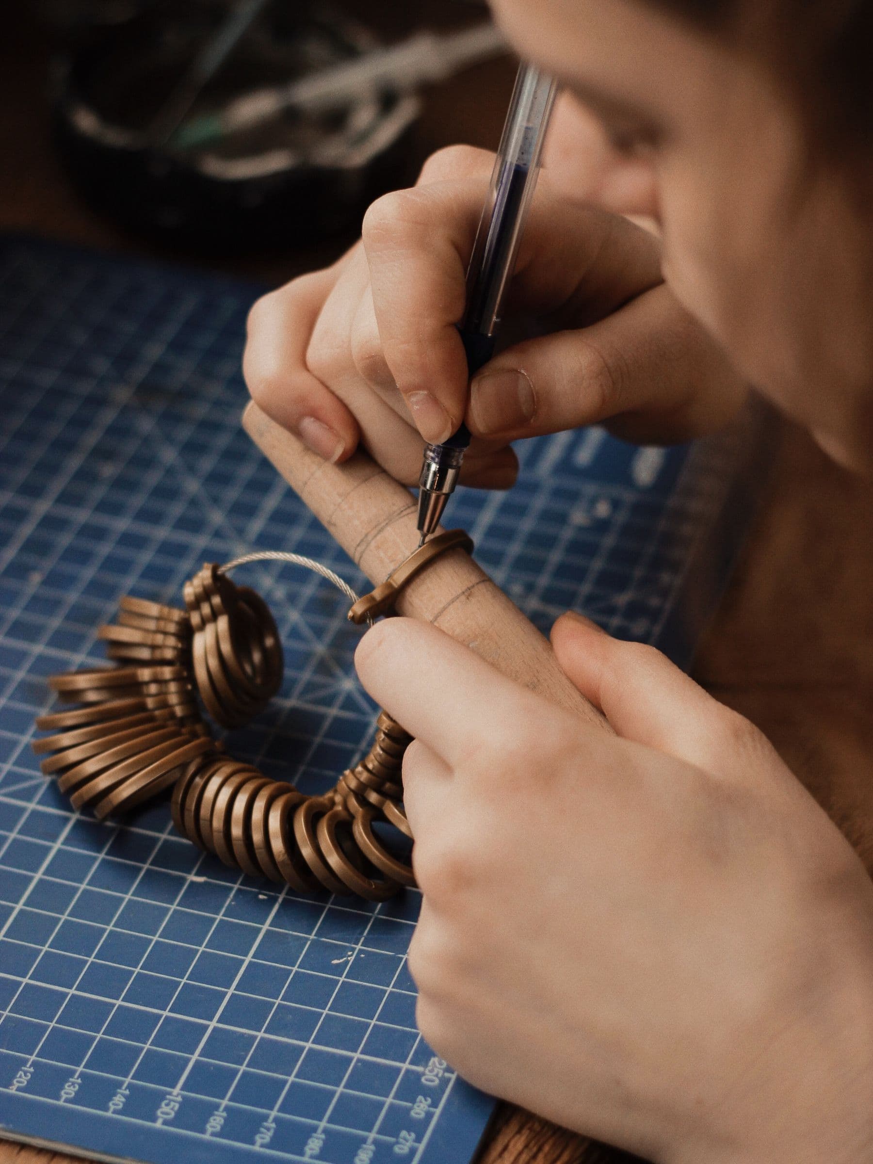 Hands checking a ring against a set of ring sizing gauges on a cutting mat.