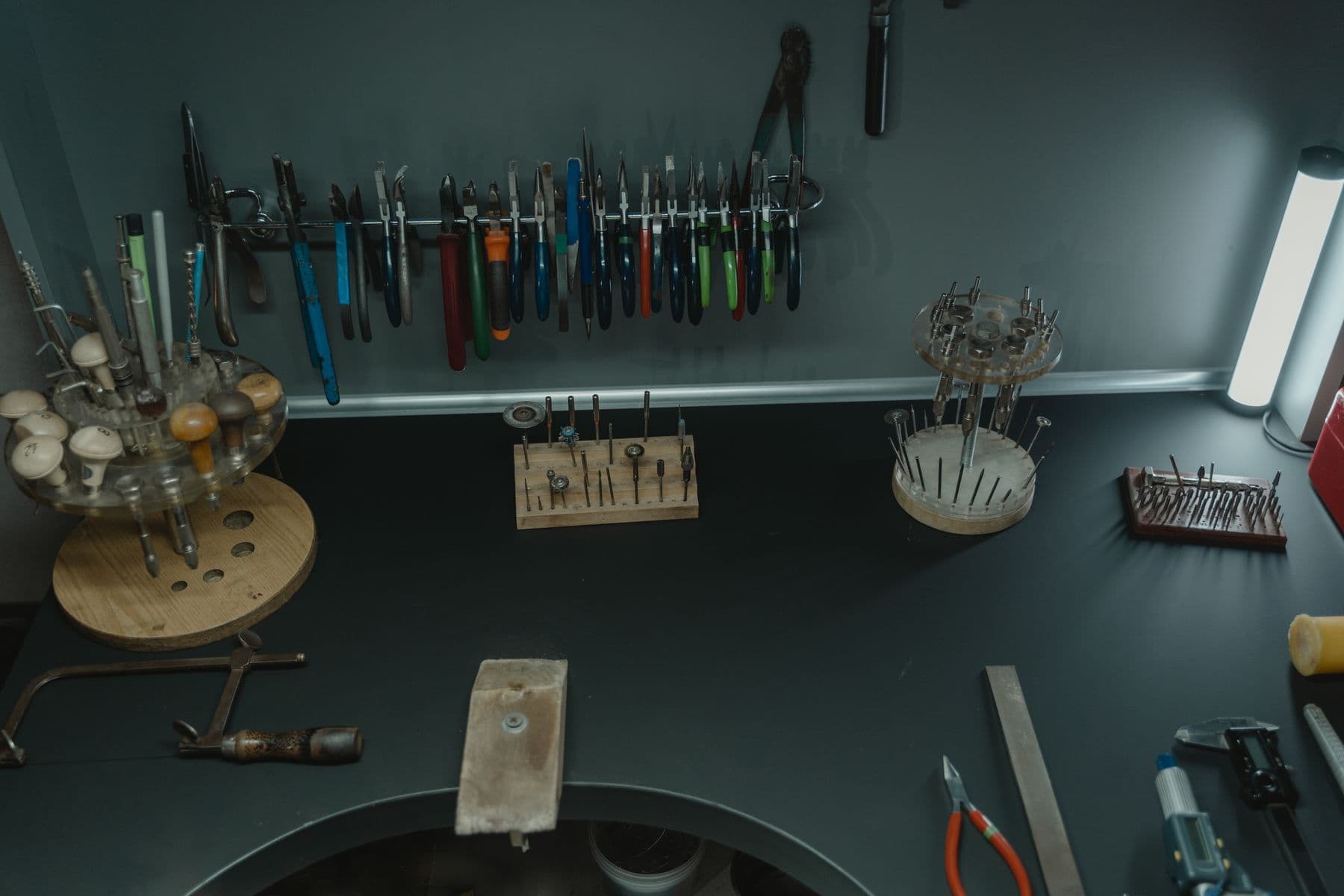 A jeweler's bench from above, with pliers and burs racked along the wall.